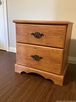 Front angle view of the wooden end table showing two drawers with dark metal handles and scalloped base detail.