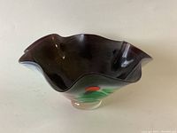 Dark art glass bowl with wavy rim and decorative accents, shown against a plain background