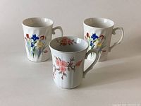 Set of three mugs showing floral designs on white porcelain