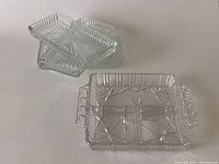 Four rectangular clear crystal glass serving dishes arranged overlapping, showing ridged edges and starburst pattern bases.