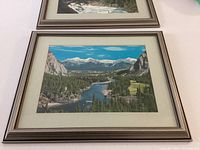 Framed landscape print showing a river winding through a valley with mountains in the background.