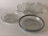 Photo showing three glass serving dishes including a rectangular dish with decorative leaf pattern and two round three-sectioned dishes, one larger with silver-tone rim and one smaller without.