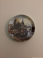 Decorative plate depicting a boy and a cabin near a river by trees and clouds.