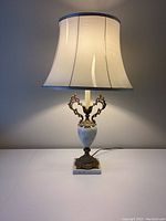 Full view of lamp with cream fabric bell-shaped shade showing tear, marble base, and bronze ornate handles.