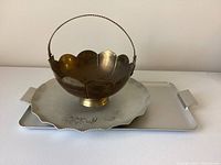 Brass bowl with scalloped edge and twisted wire handle placed on rectangular metal tray