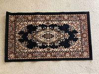 Black and brown rectangular rug with a central floral medallion design and intricate borders.