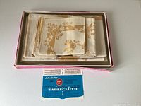 Boxed set containing folded oblong tablecloth and matching napkins with original label showing product info.