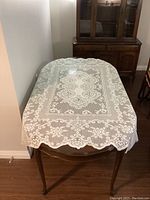 Oval lace tablecloth on wooden table showing detailed floral lace pattern with scalloped edges