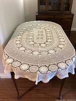 Oval ecru crocheted tablecloth laid on a table, showing overall pattern and size