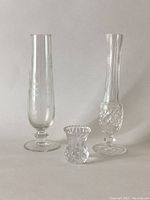 Photo showing three clear glass vases: two tall ones about 9 inches high with different patterns, and one small textured vase about 2.5 inches high.