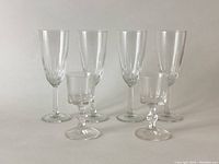 Four tall wine glasses and two liqueur glasses shown together on neutral background