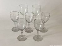 Front view of seven clear wine glasses, showing five with flower etched pattern and two plain behind