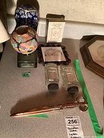 Overview of the assortment of various home decor items on a beige table showing two decorative candle holders, two glass shakers, a metal letter opener, a clock box, and other items.