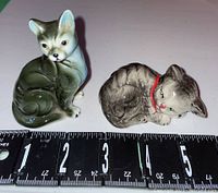 Front view of two cat figurines on white background with ruler for size reference