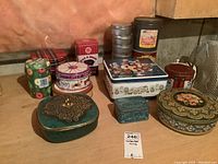 Various vintage collector tins on concrete floor against wall, differing in shape, size, and colors