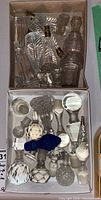 Boxes of assorted clear, frosted, and blue glass decanter stoppers and glass lighting accessory pieces photographed from above.