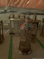 Brass decanter caddy with three clear glass bottles with brass lids and two separate glass decanters with brass trimmings, on a table in basement