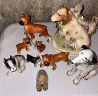 Overview of nine ceramic dog figurines, showing various sizes and breeds with one large dog and fence figurine and eight smaller ones.