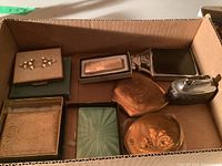 Overview photo of all items in a cardboard box showing various vintage lighters, pill boxes, and trinket boxes.