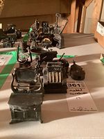 Photo of a lineup of various metal miniature pencil sharpeners with a focus on the front items including a table and cash register.