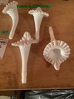 Four white milk glass floral-shaped flower frogs displayed on a wooden surface, clear view of ruffled edges and hobnail texture, matching seller's description and condition.