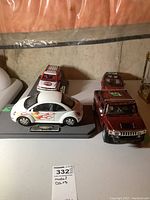 White Volkswagen Beetle model car with flames, mounted on a labeled base next to red Hummer H2