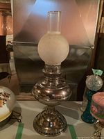 Full view shot of the oil lamp showing gold tone metal base with frosted glass globe on top