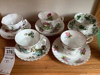 Five sets of porcelain teacups and saucers arranged on wooden surface showing varied floral patterns and shapes.
