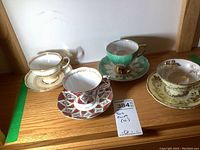 Four teacup and saucer sets with different floral and gold designs, arranged side by side