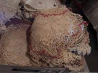 Pile of off-white and cream crocheted doilies with red trim