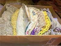 Box filled with folded crocheted and embroidered vintage tablecloths and doilies in various colors and patterns.