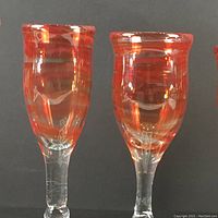 Close-up of two hand-blown flute glasses showing red and orange swirl design on bowl, clear base and stem.