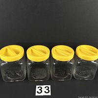 Front view of 4 square glass jars with yellow ribbed plastic lids displayed in a row, showing embossed floral designs and lettering 'RICHE'