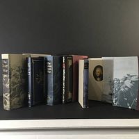 Side view of 7 Folio Society books with visible titles and slipcases showing war-related art and photography.