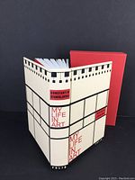 Book from angle showing front cover and open pages, alongside red slipcase.