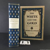 Front cover of the book with visible gold and white fleur-de-lis design on spine next to slipcase showing title and author label.