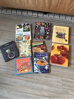 Top view of nine vegetarian and vegan cookbooks arranged on floor showing colorful covers with vegetable and dish imagery.
