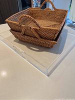 Stack of two woven square baskets with handles placed on top of one clear acrylic tray.