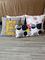 Group of four casual decorative cushions showing different colors and patterns including letter E, floral prints, and colorful abstract shapes.