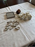 Photo showing three different sets of napkin rings: silver-tone metal, white beaded, and tortoiseshell plastic, spread out on a cloth surface.