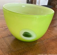 Front side view of apple green hand blown glass bowl sitting on wooden table, showing vibrant smooth finish with lighter and darker green shading.