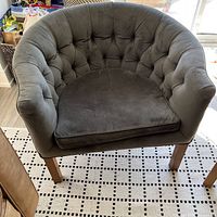Front angle view of the dark grey tufted curved tub chair showing full shape, cushion, and wooden legs.