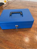 Closed blue Helix lock box with black handle and key lock on wooden table.