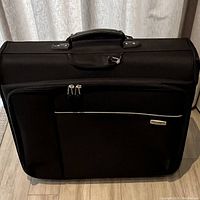 Front view of black rolling garment bag with large outer pocket and top handle visible