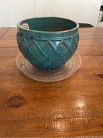 Teal ceramic planter pot showing rounded shape, lattice diamond texture pattern and glossy teal enamel finish from front angle. Clear plastic drip tray seen underneath pot.