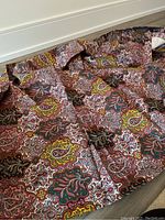 Folded tablecloth spread on floor showing overall paisley pattern in multiple colors including red, yellow, green, black and white.
