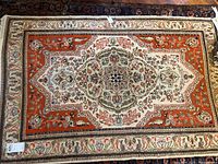 Full view of the rug showing the geometric floral medallion pattern and orange border with floral motifs.