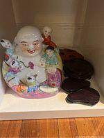 Colorful ceramic Laughing Buddha figure with children and several wooden stands.