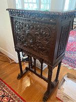 Side view of ornate carved wood cabinet showing detailed leaf and floral accents, supported by twisted spindle legs and carved feet.
