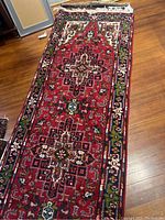 Full view of red Persian style geometric pattern carpet runner laid on wooden floor.
